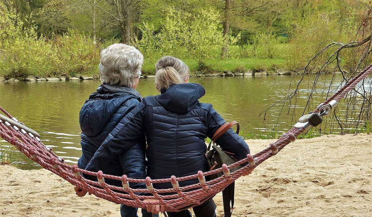 Zwei Frauen sitzen draußen auf einer Hängematte.